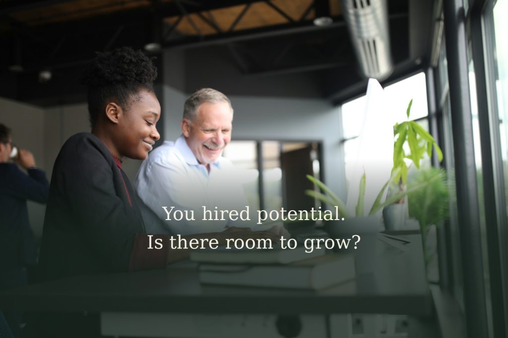 Two colleagues working together at a computer, with the text "You hired potential. Is there room to grow?"