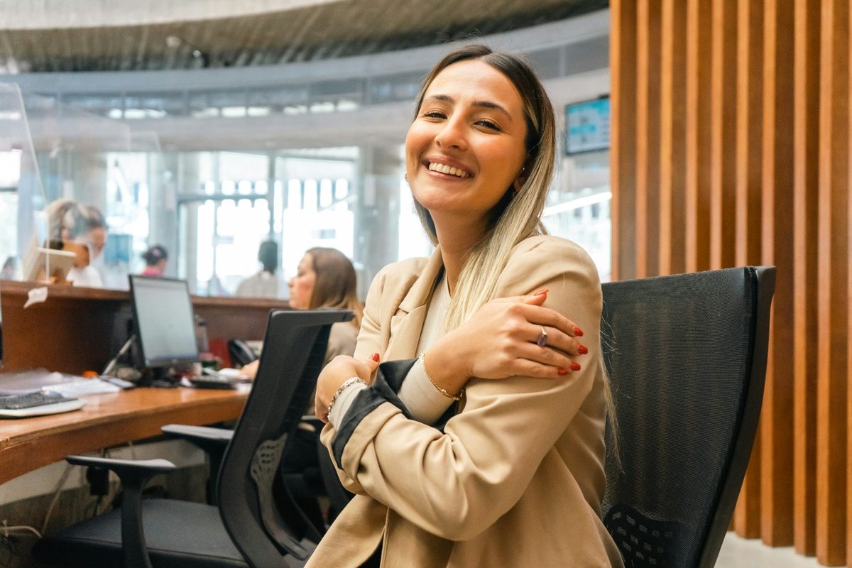Smiling employee in a beige blazer seated at her workstation in a bright open office